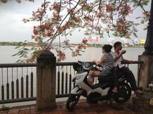 A couple eating their lunch on a motorcycle by the river.