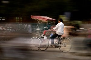 photo of a cyclo rider on a blurred and busy street